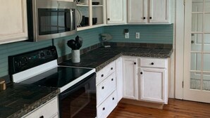 Una cucina con mobili bianchi, un piano cottura nero e un rivestimento a parete color petrolio.