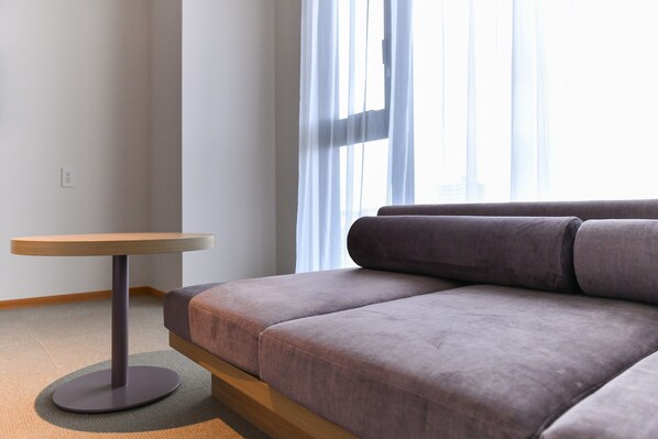 Una sala moderna con un sofá gris, una mesita redonda y cortinas de gasa.
