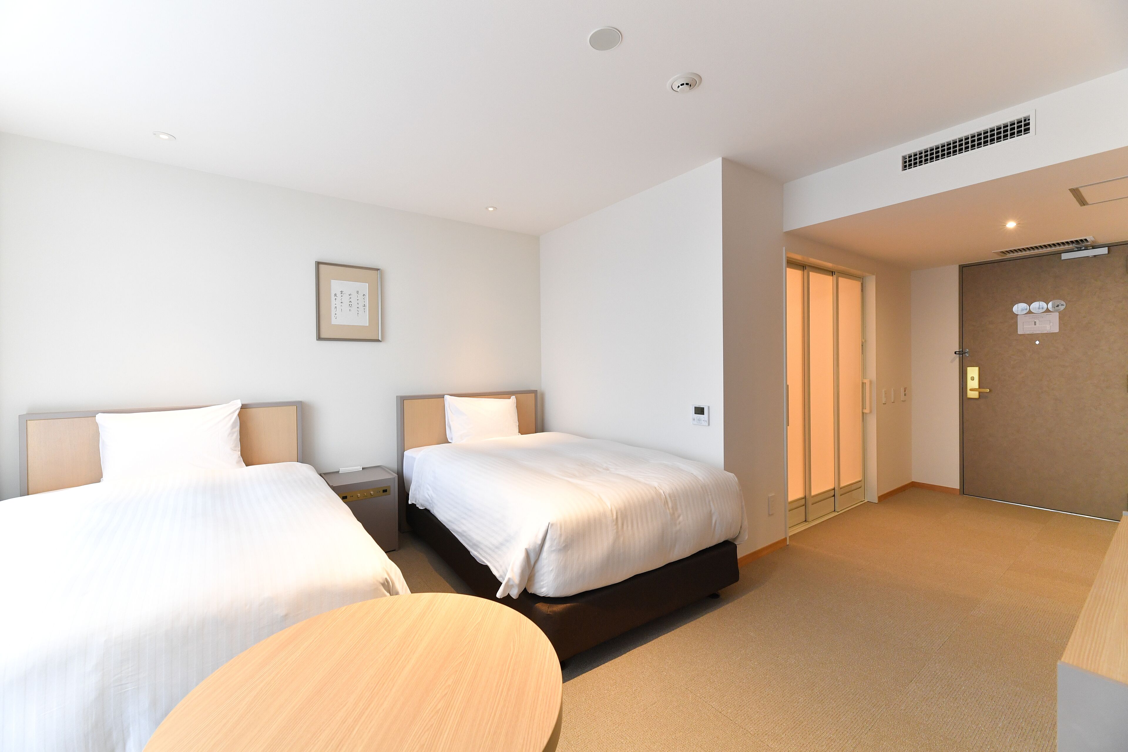 Una habitación de hotel con dos camas, una mesa redonda y una puerta que da a otra habitación.
