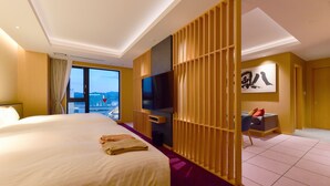 Quarto de hotel com cama grande, televisão, sofá e vista para a cidade.