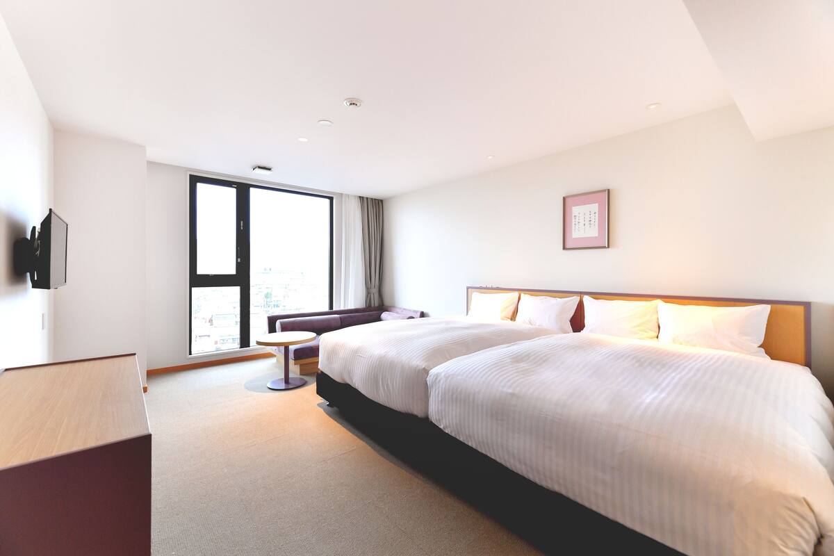 A modern hotel room with a large bed, a sofa, a small table, and a TV.