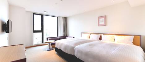 A modern hotel room with a large bed, a sofa, a small table, and a TV.