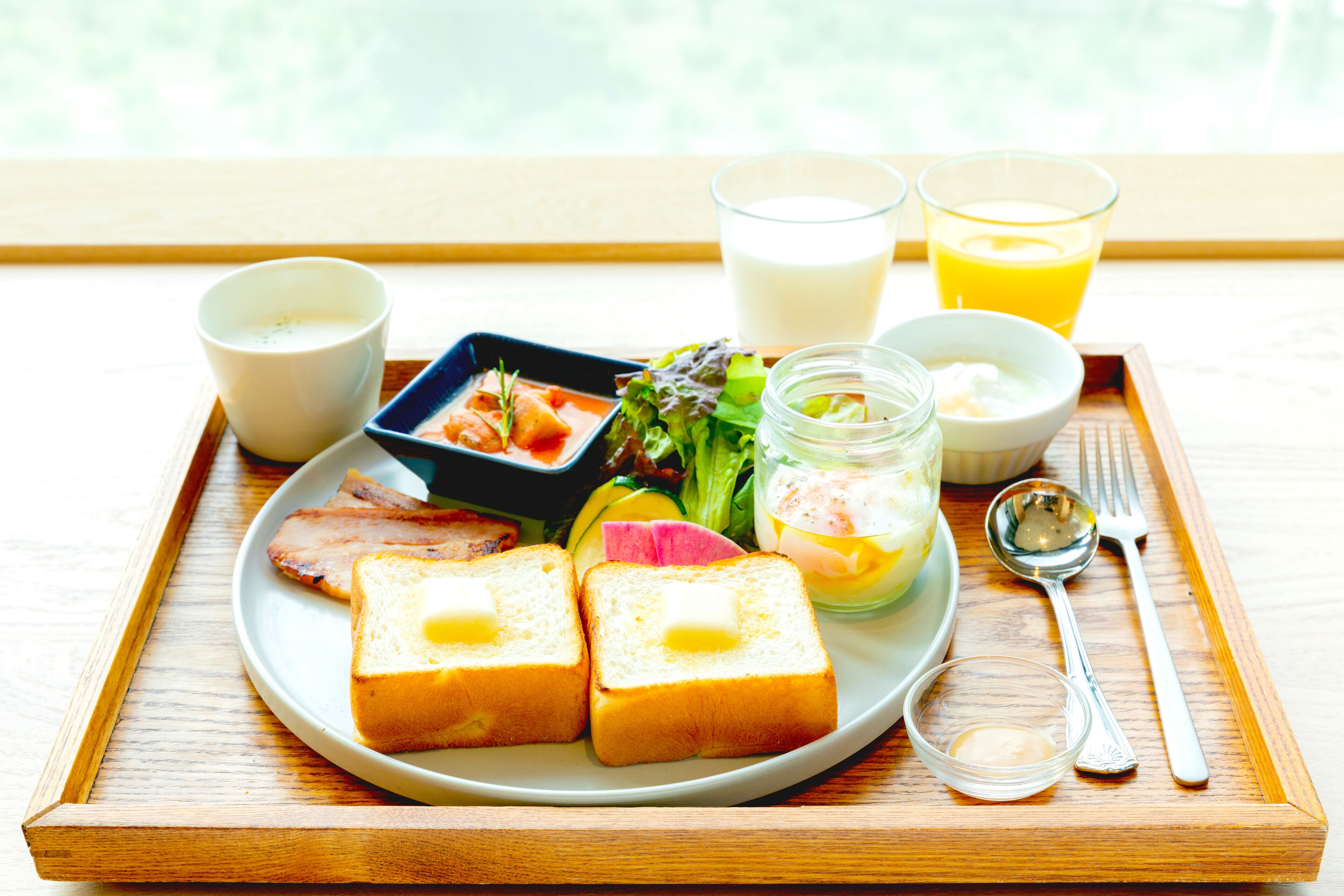 A breakfast tray with toast, eggs, vegetables, and drinks on a wooden table.