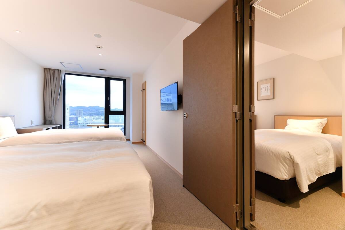 A hotel room with two beds, a television, and a city view.