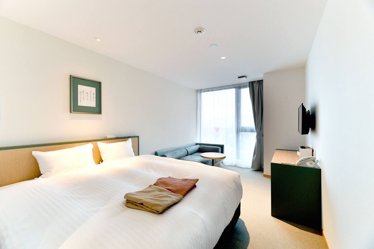 A hotel room with a large bed, a sofa, a desk, and a TV.