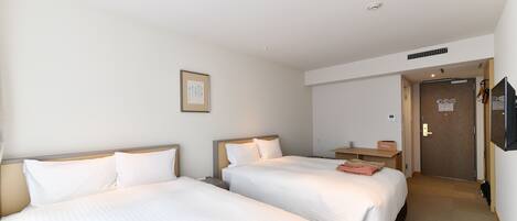A hotel room with two beds, a wooden headboard, a bedside table, a TV mounted on the wall, and a door leading to a bathroom.