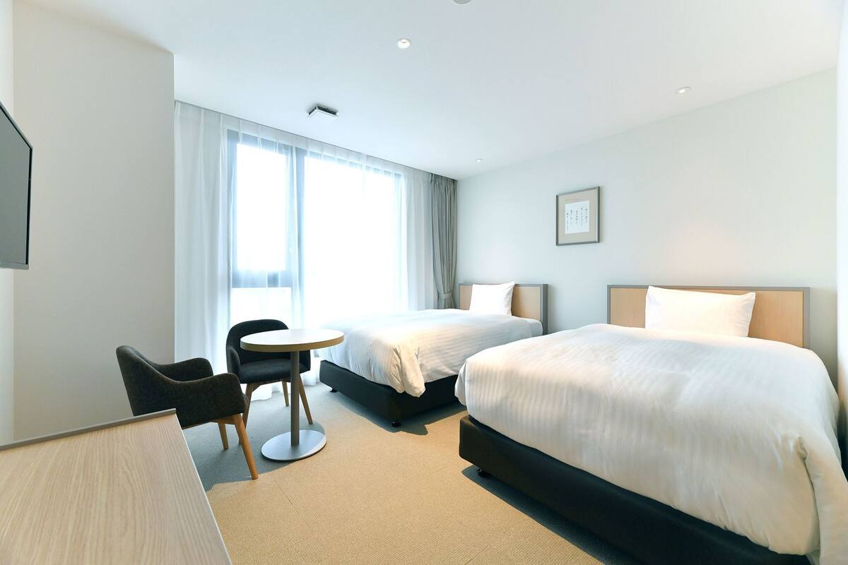 A hotel room with two beds, a desk, a chair, and a window with curtains.