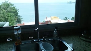 A kitchen with a sink and a window overlooking a body of water and distant buildings. - Luxury Beachfront Condo with Amazing Ocean Views (Gorgona)