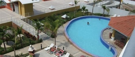 A pool area with lounge chairs and a view of the ocean.