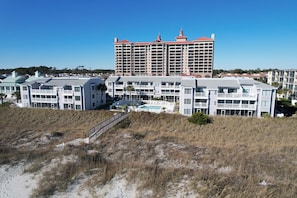 Um hotel na praia com várias varandas, uma piscina e um edifício grande ao fundo.