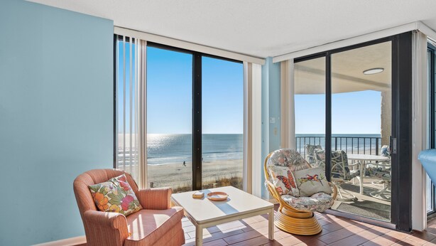 Una habitación con vista a la playa, una silla, una mesa y un sillón de mimbre.