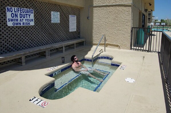 A man in a small pool with a sign stating "NO LIFEGUARD ON DUTY SWIM AT YOUR OWN RISK."