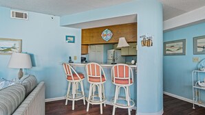 Un espacio habitable compacto con kitchenette, una zona de comedor con taburetes de bar, un sofá y una lámpara.