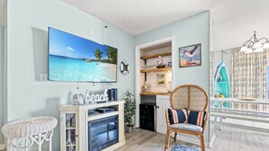 A living room with a flat-screen TV, wicker furniture, a bookshelf, and a view of the ocean. - Sea Castle 2F-Oceanfront 3 Bedroom- Pool & Hot Tub (North Myrtle Beach)