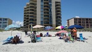 A beachfront hotel with multiple balconies, beach umbrellas, and beach chairs. - Sea Castle 2F-Oceanfront 3 Bedroom- Pool & Hot Tub (North Myrtle Beach)