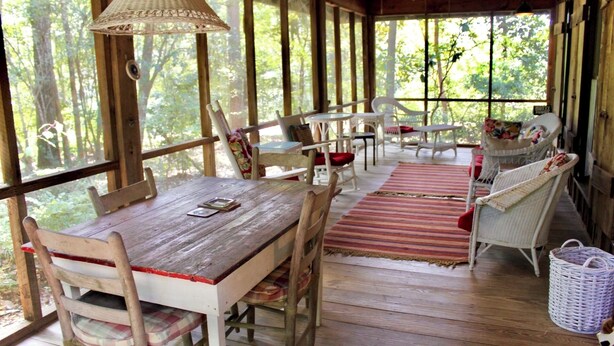 A wooden deck with a table and chairs, surrounded by large windows offering a view of the forest.