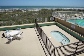 A rooftop pool area with a hot tub, lounge chairs, and a view of the beach.