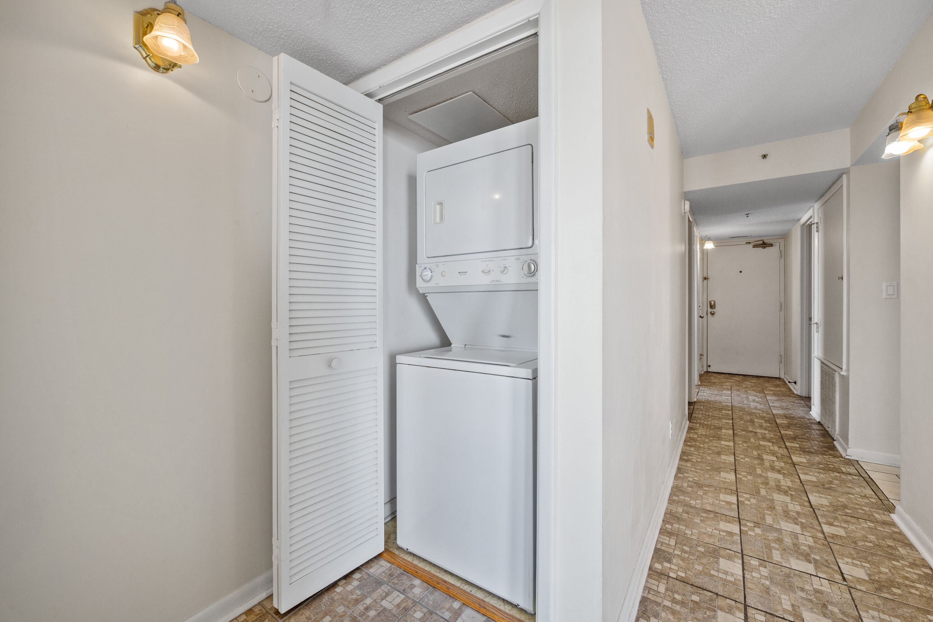 A laundry room with a washer and dryer, a white door, and a hallway with a tiled floor.