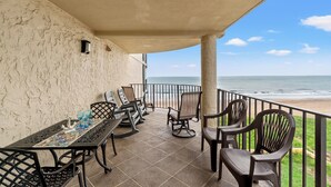 Un porche cubierto con una mesa y sillas, vista a la playa y una barandilla.