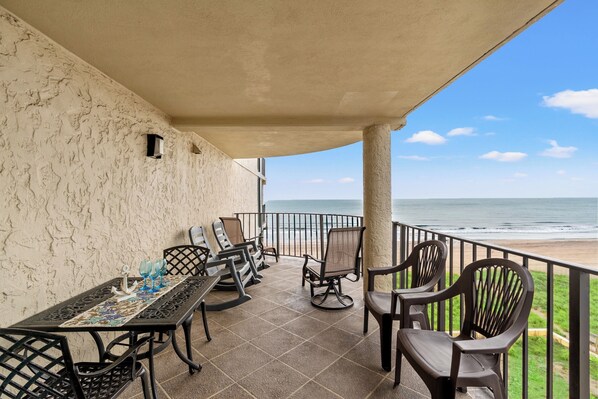 Une terrasse couverte avec une table et des chaises, une vue sur la plage et une rambarde.