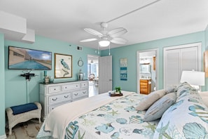 Une chambre à coucher comprenant un lit, un ventilateur de plafond, une commode, un banc et un téléviseur fixé au mur.