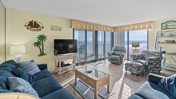 Un salón con sofá, sillones, una mesa de centro, televisión y un balcón con vistas.