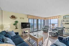 Un salón con sofá, sillones, una mesa de centro, televisión y un balcón con vistas.