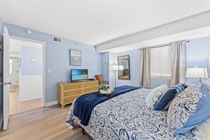 Een slaapkamer met een bed, een kaptafel, een televisie en een deur naar een andere kamer.
