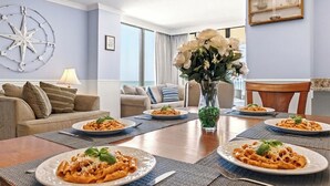 Een eetgedeelte met een tafel gedekt voor vier personen, met borden pasta, een vaas met bloemen en een kompasdecoratie aan de muur.