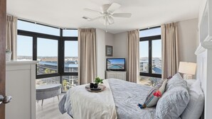 Ein Schlafzimmer mit einem großen Bett, einem Deckenventilator, einem Fernseher und Blick auf einen Swimmingpool und Gebäude.