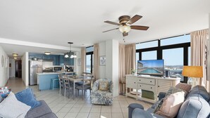 Ein modernes Wohnzimmer mit einer Couch, einem Essbereich mit Tisch und Stühlen, einer Küche mit Kühlschrank und Mikrowelle sowie einem großen Fenster mit Blick.