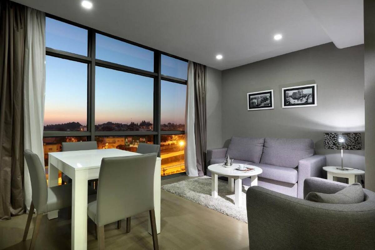 A modern living room with a dining area, large windows with a city view, and two framed pictures on the wall.