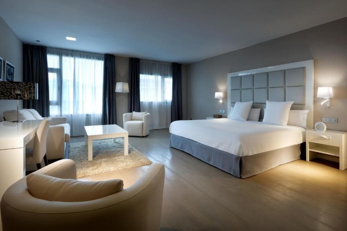 A modern hotel room with a large bed, a desk, a chair, and a sofa.