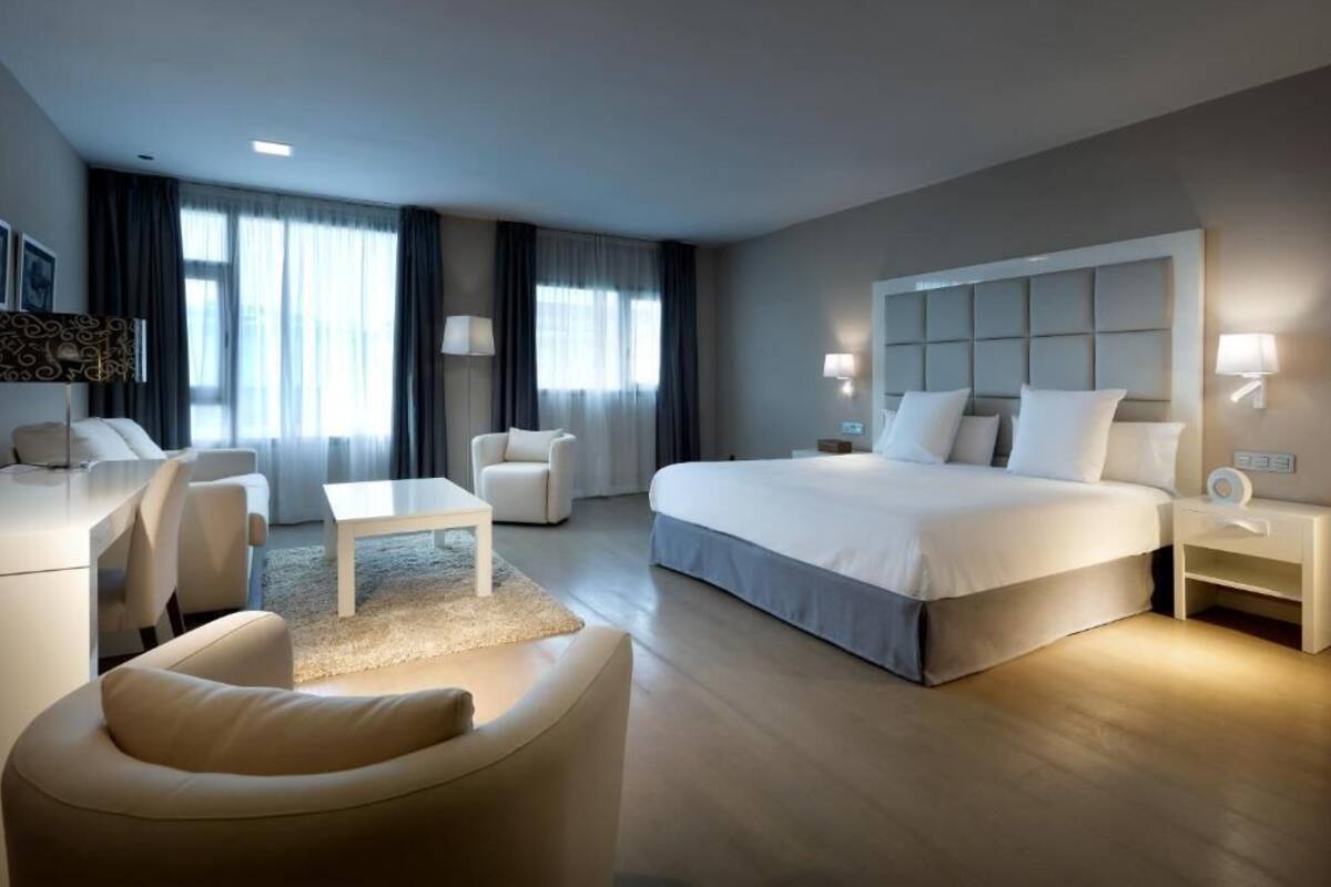 A modern hotel room with a large bed, a desk, a chair, and a sofa.