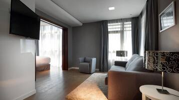 Un salon moderne avec un téléviseur à écran plat fixé au mur, un canapé, un fauteuil et une petite table avec une lampe.