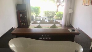 A bathroom with a freestanding bathtub, a wooden vanity, and a television on a shelf. - SV Boutique Resort (Vung Tau)