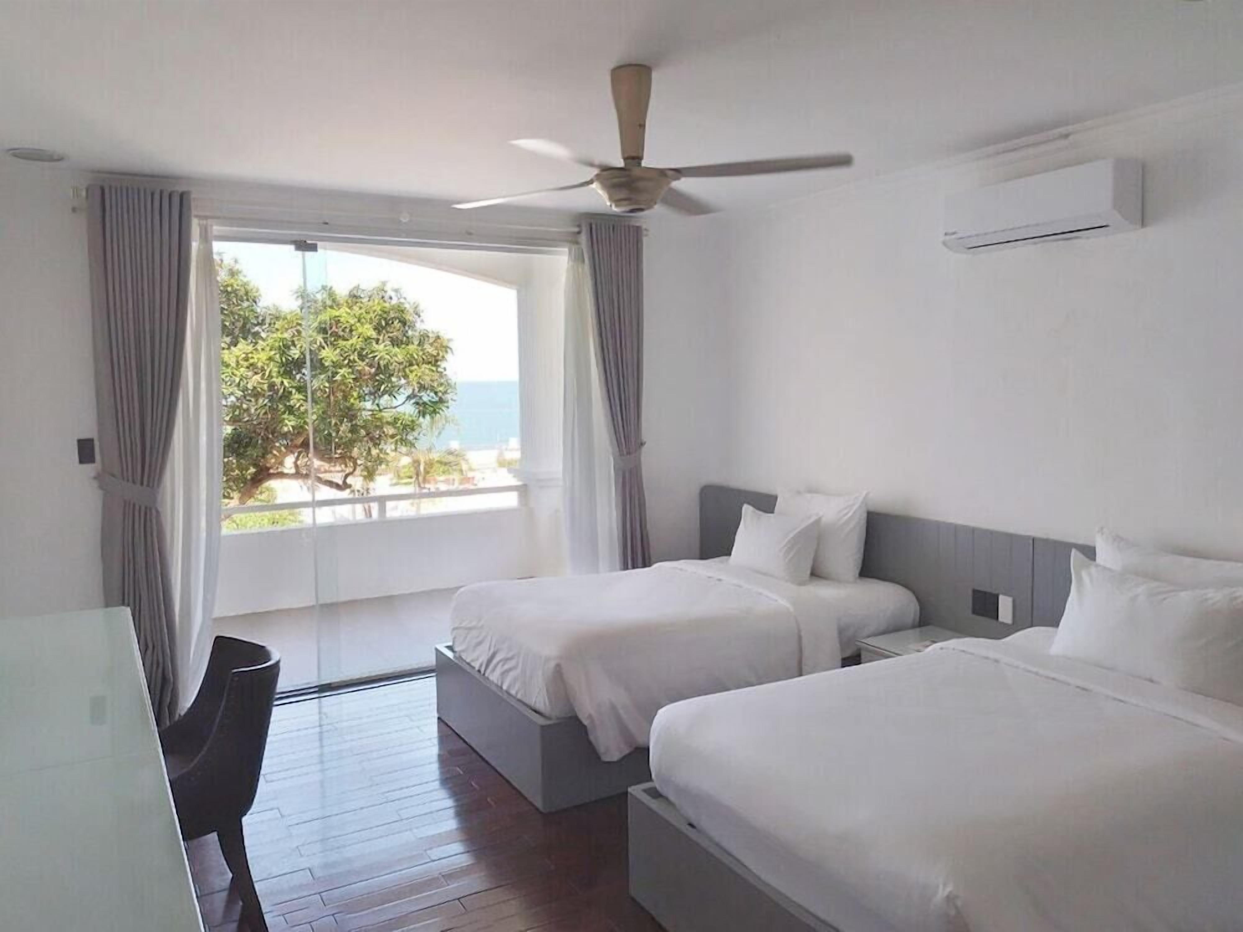 Ein Hotelzimmer mit zwei Betten, einem Deckenventilator und Meerblick.