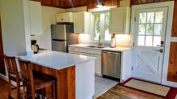 A compact kitchen with white cabinetry, a stainless steel refrigerator, a dishwasher, and a wooden island with bar stools. - Beautiful Water Views, Huge Yard, Boat Dock, Private, Quiet, Minutes to Beaufort (Beaufort)