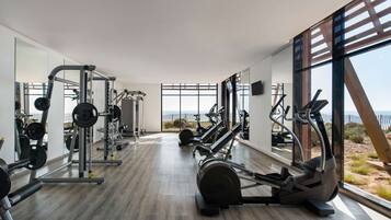 A modern gym with various exercise equipment, large windows, and a wooden floor.