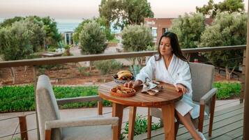 A woman sitting at a wooden table on a deck with a view of the ocean and trees.