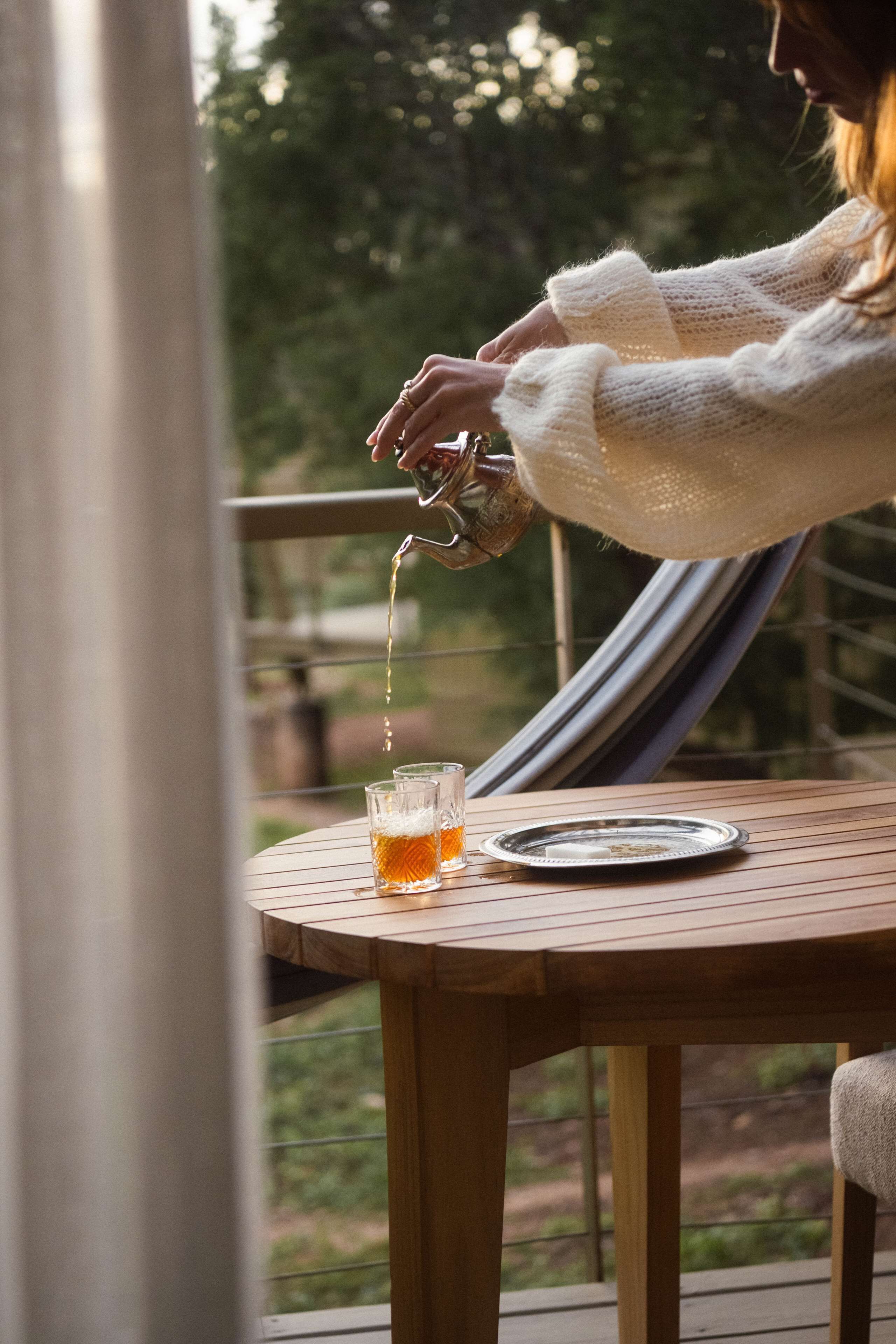 Iemand giet een drankje in een glas op een houten tafel, buiten.