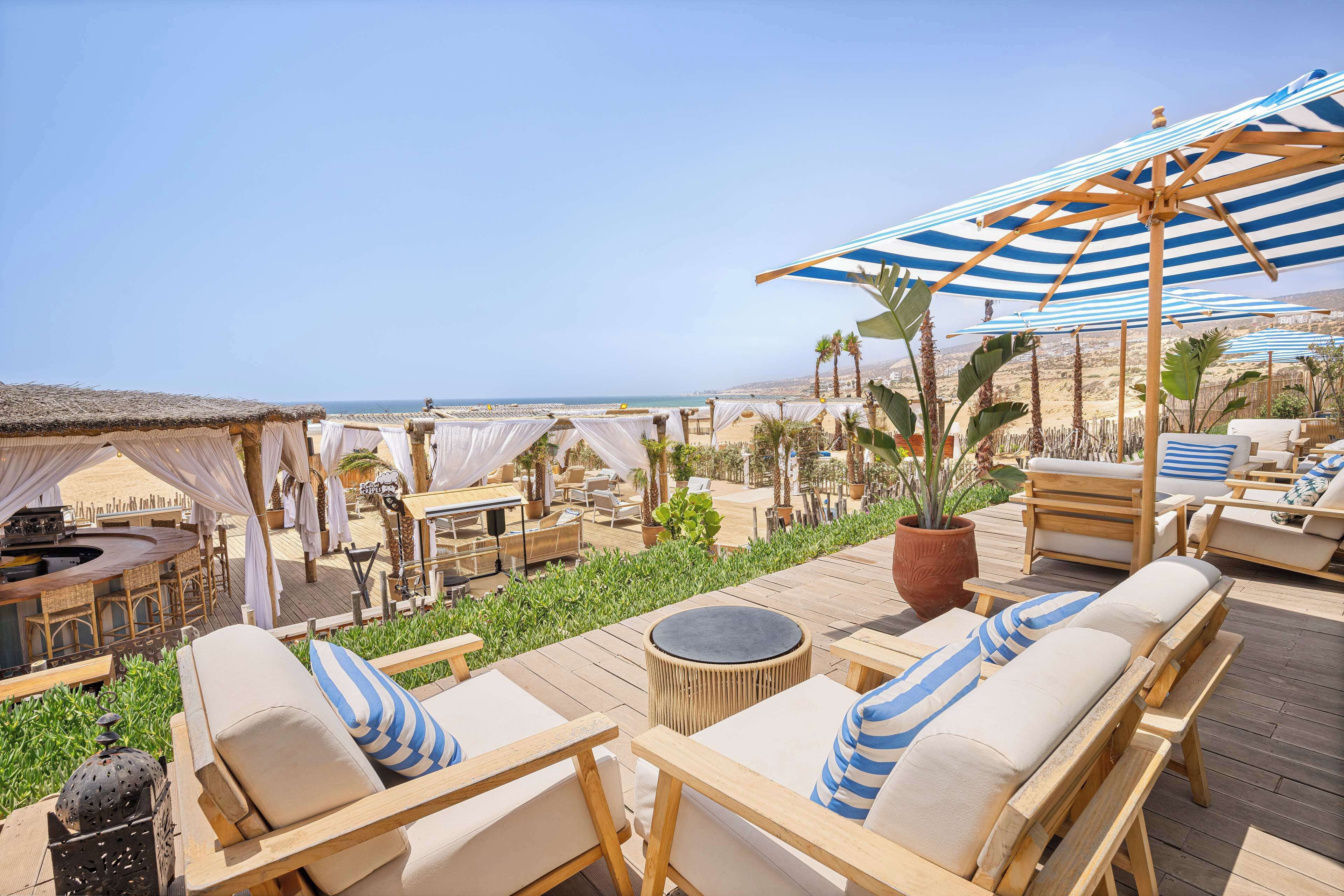 Un espace bar aménagé sur le toit, avec des meubles en bois, des coussins à rayures et une vue sur la plage.