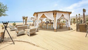 A beachside resort with a wooden deck, lounge chairs, a bar area, and a thatched-roof gazebo. - Radisson Blu Resort, Taghazout Bay Surf Village (Taghazout)
