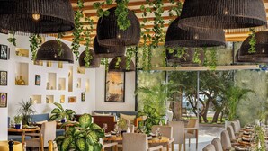 A restaurant with wicker ceiling lamps, indoor plants, and a view of the outdoors. - Radisson Blu Resort, Taghazout Bay Surf Village (Taghazout)