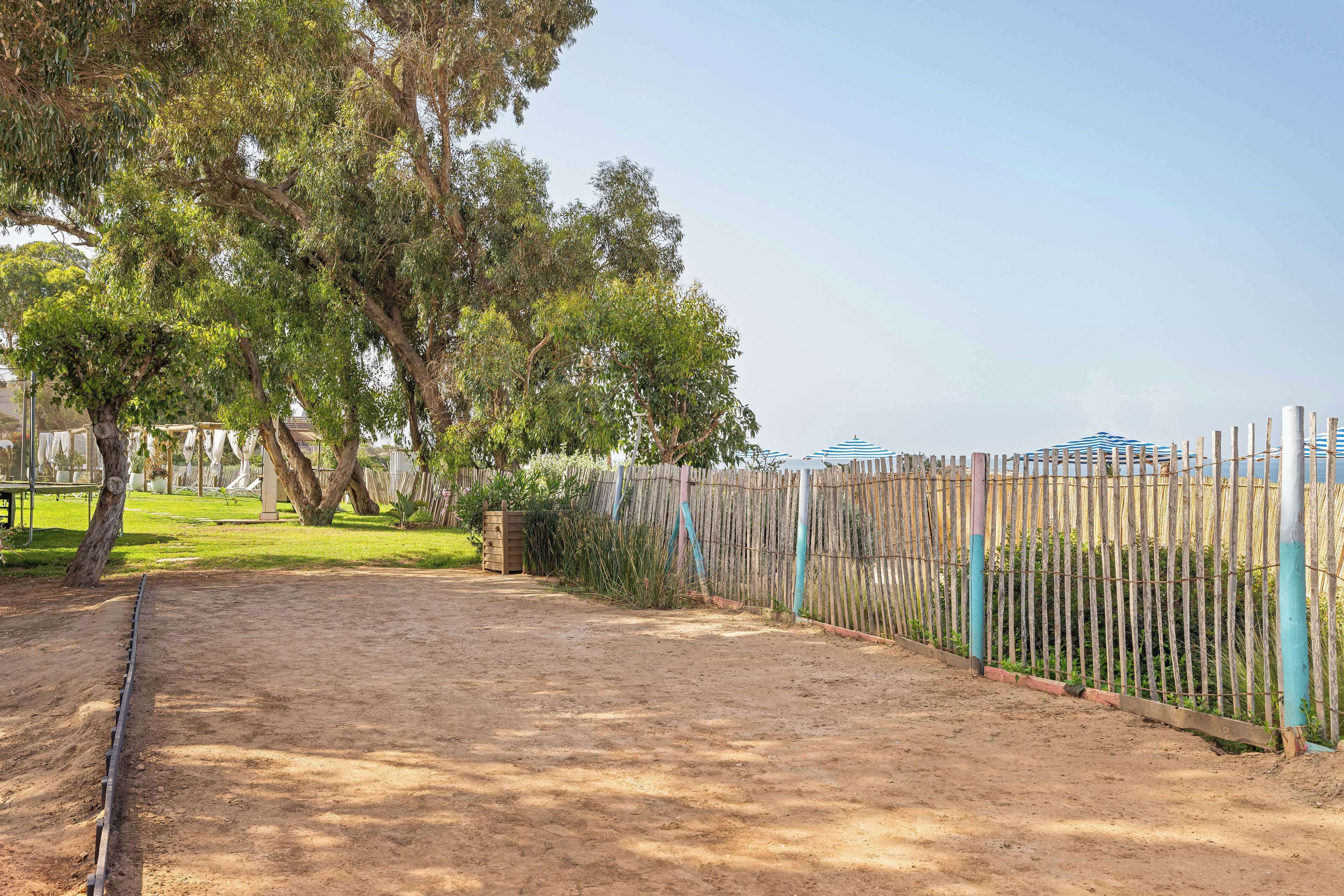 A fenced outdoor area with a dirt path, trees, and a clear sky.
