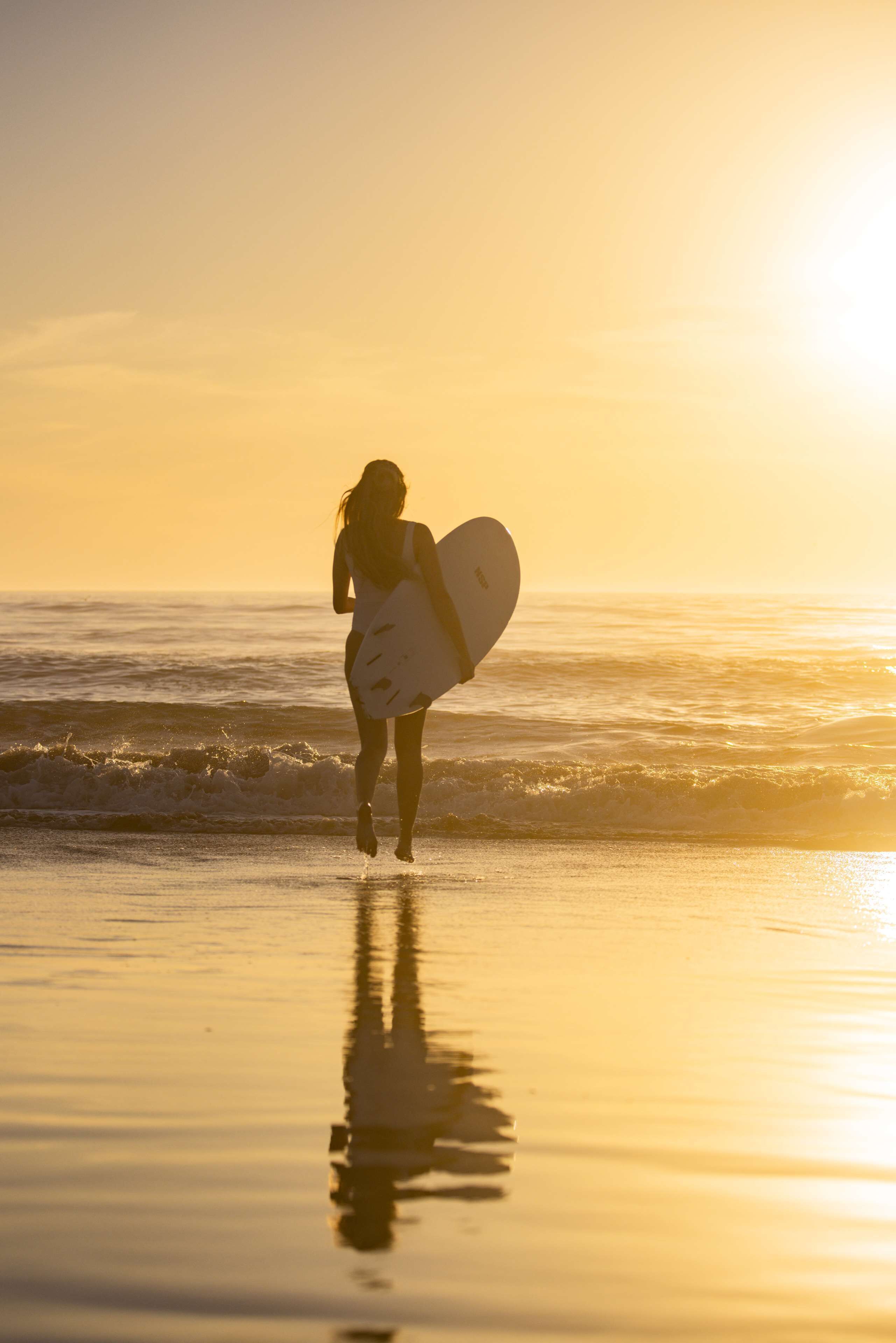 A person carrying a surfboard on a beach during sunset.