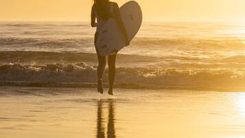 A person carrying a surfboard on a beach during sunset.