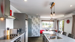 A modern kitchen with a central island, stainless steel appliances, and a dining area with a view. - Sunshine and Snow Lodge - Ohakune Holiday Home (Ohakune)