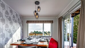 A dining area with a table set for six, a red bean bag, and a view of the outdoors through a large window. - Sunshine and Snow Lodge - Ohakune Holiday Home (Ohakune)