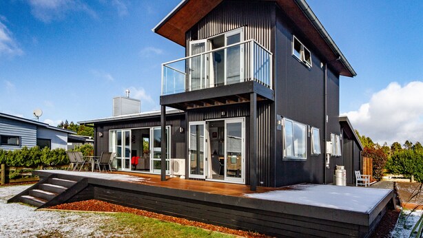 A modern two-story house with a balcony, large windows, and a wooden deck. - Sunshine and Snow Lodge - Ohakune Holiday Home (Ohakune)
